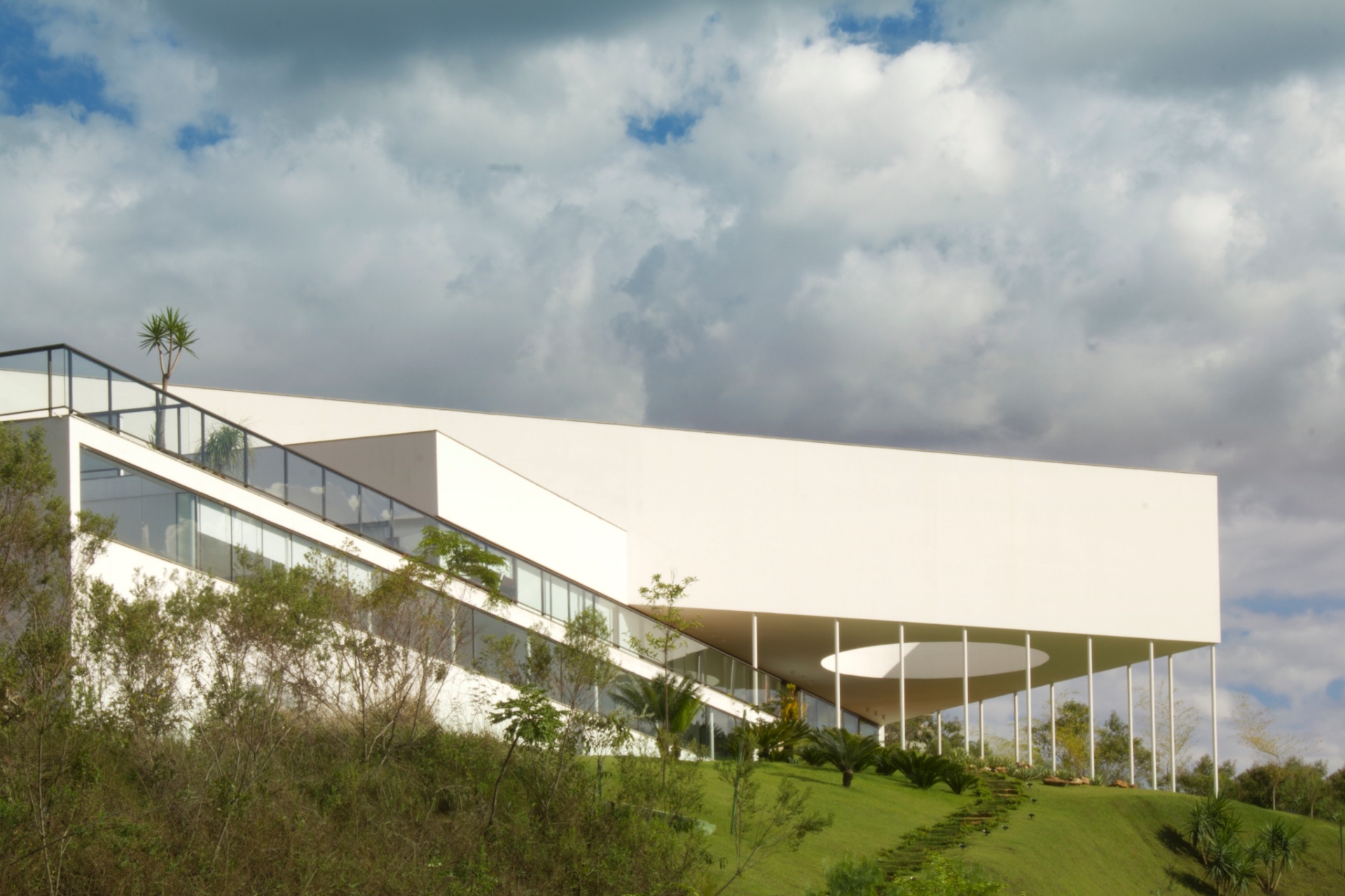 A Casa Galeria, assinada pela MACh Arquitetos, é composta de um bloco retangular longitudinal, paralelo à via de acesso, que dá base a um volume triangular elevado do solo, sustentado pela sucessão de delgados pilares metálicos preenchidos por concreto. A própria sobreposição de volumes geométricos e recortes de vãos, que criam jogos de luz natural e integram os interiores ao entorno, faz do design obra de arte - Gabriel Castro/ Divulgação