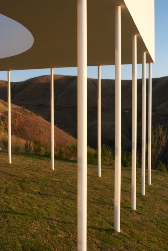 Delgados pilares metálicos sustentam o bloco triangular superior que forma, ao mesmo tempo, o terraço da área íntima do pavimento superior e a cobertura da varanda frontal e térrea da Casa Galeria. Os pilares são preenchidos com concreto e ancorados em fundações escondidas sob a grama. O desenho respeita a inclinação natural do terreno e tem assinatura dos arquitetos Fernando Maculan e Mariza Machado Coelho - Fábio Del Re & Carlos Stein/ Divulgação