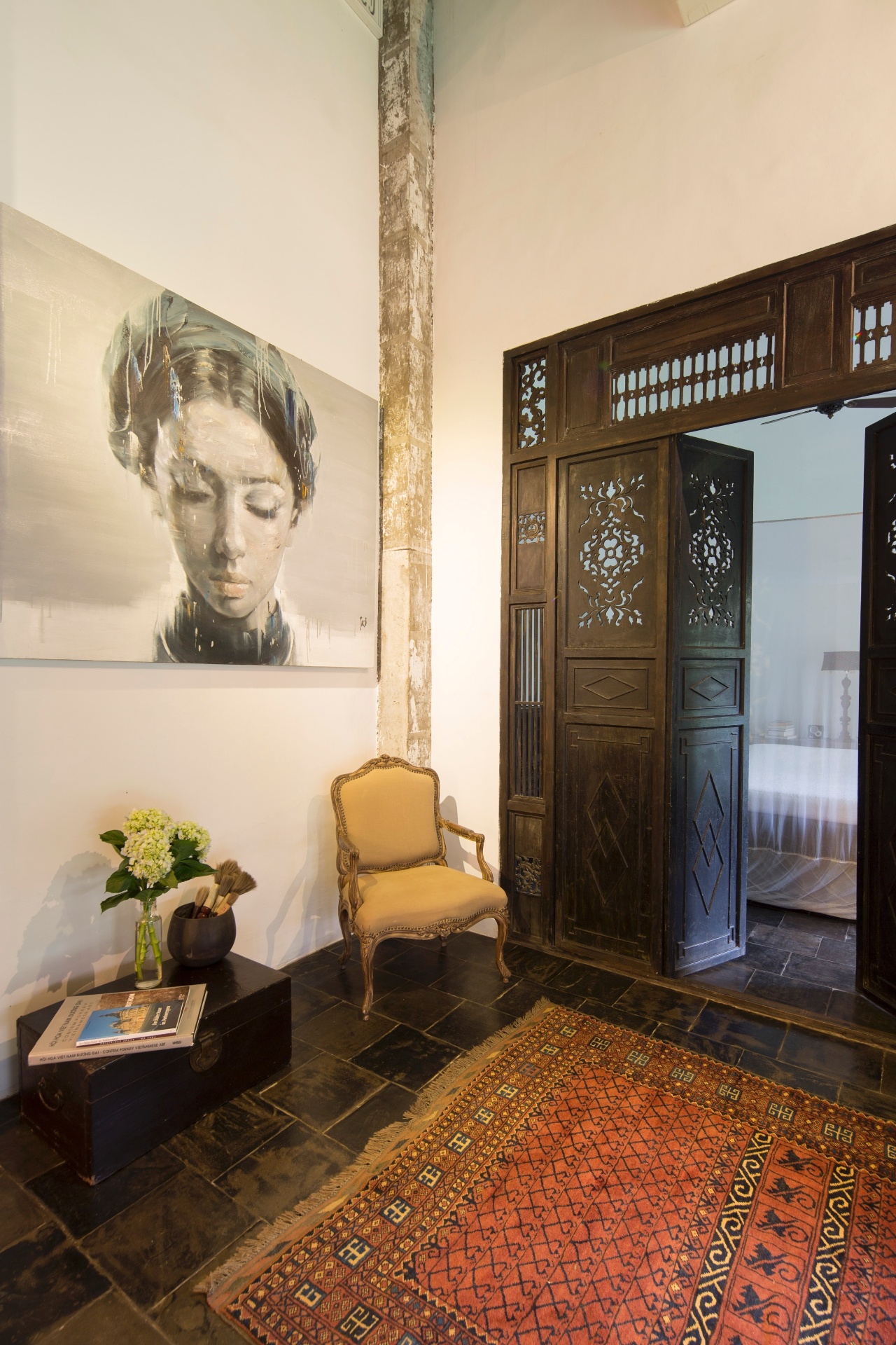 (Imagem do NYT, usar apenas no respectivo material) As portas de madeira com intrincados entalhes e recortes presta homenagem ao passado colonial francês de Ho Chi Ming, bem como as malas (à esq.), que fazem as vezes de mesa de apoio. Ainda no ambiente, a pintura de Phuong Quoc Tri (à esq.), um artista vietnamita, é combinada à cadeira estilo Luís 15 e ao tapete paquistanês - Marcel Lam/ The New York Times