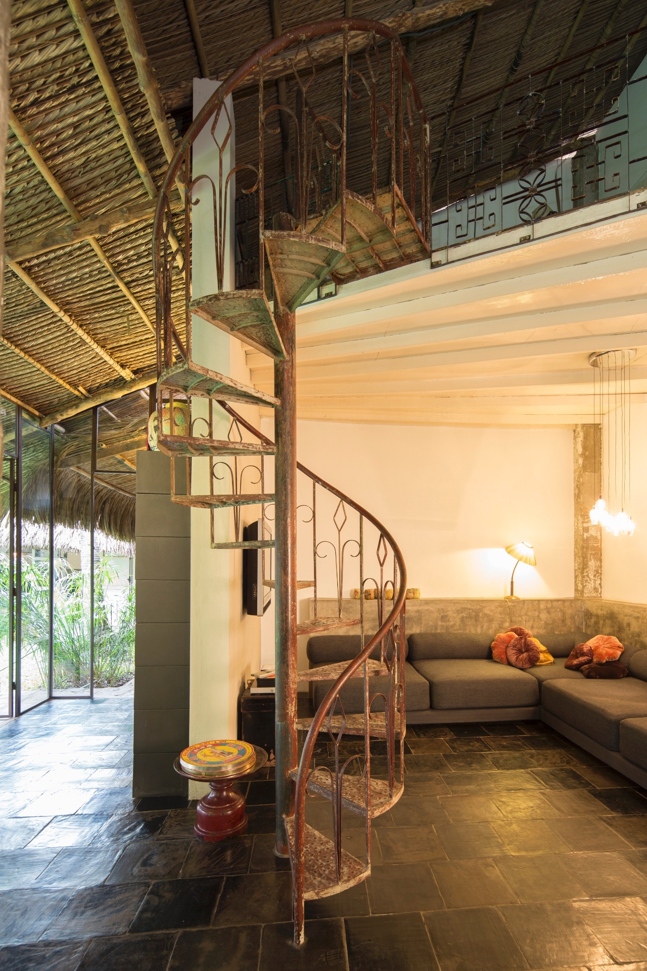 (Imagem do NYT, usar apenas no respectivo material) Hedwig Pira desenhou o sofá do living (à dir.), feito localmente. Sobre o móvel, a luminária pendente é da Habitat e foi comprada na Bélgica. Ao lado da escada caracol (à esq.) está uma pequena mesa antiga e comumente utilizada para fazer oferendas ao Buda - Marcel Lam/ The New York Times