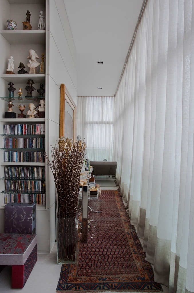 O pilar estrutural revestido com laminado foi aproveitado para a instalação de duas estantes, dispostas em extremidades opostas. Em uma delas, parte das prateleiras apoiam a coleção de Napoleões, livros e CDs do morador. No corredor lateral, o designer de interiores Oscar Mikail que assina o projeto de reforma, colocou um aparador que serve como mesa-bar. No chão, destaque para a passadeira caucasiana. As cortinas de linho foram confeccionadas por Mônica Bagatelli - Thiago Travesso/ Divulgação