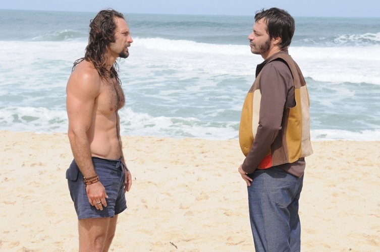 O personagem Carlão (Fernando Pavão), em cena da novela "Pecado Mortal", na fase da década de 1970, usa short na praia contracenando com o policial Van Gogh (Heitor Martinez)