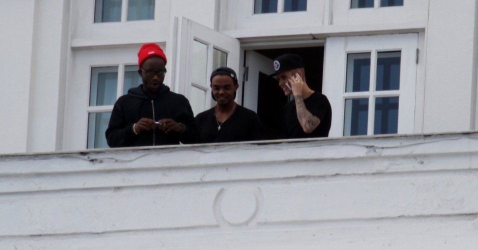 1.nov.2013 - Sem casaco e com outro boné, Justin Bieber volta para a sacada do Copacabana Palace falando no celular