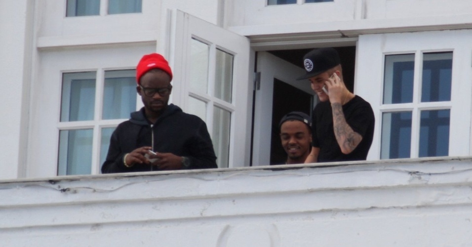 1.nov.2013 - Sem casaco e com outro boné, Justin Bieber volta para a sacada do Copacabana Palace falando no celular