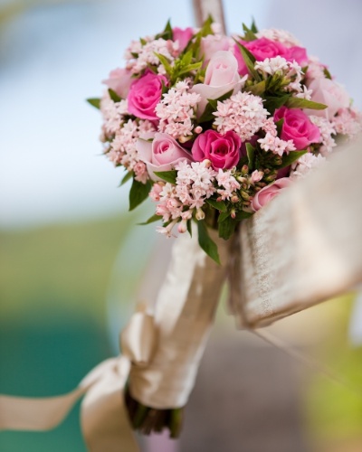 Buquê com flores em tons de rosa e haste envolta por fita de cetim com laço no final