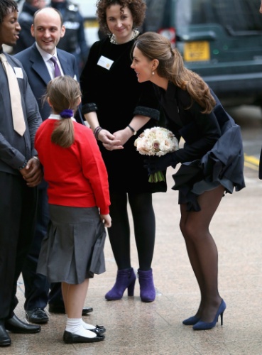20.nov.2013 - Ao descer do carro para cumprimentar uma criança, Kate Middleton passou por uma saia justa por causa do vento