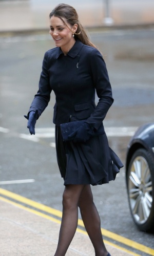 20.nov.2013 - Ao descer do carro para cumprimentar uma criança, Kate Middleton passou por uma saia justa por causa do vento