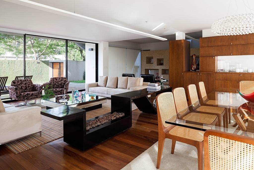 Estar e jantar se abrem para o exterior nas duas laterais, o que favorece a entrada de intensa luminosidade natural. A definição dos ambientes se dá através de um móvel-aparador desenhado pelo escritório Stuchi&Leite Projetos, responsável pela reforma. Executado em concreto com pintura preta, o móvel se destaca na Casa G+A que tem projeto original de Lemos e Corona - Ana Mello/ UOL