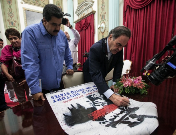 Oliver Stone (dir.) assina um cartaz da série "A História não contada dos Estados Unidos" para Nicolás Maduro, no Palácio de Miraflores, em Caracas