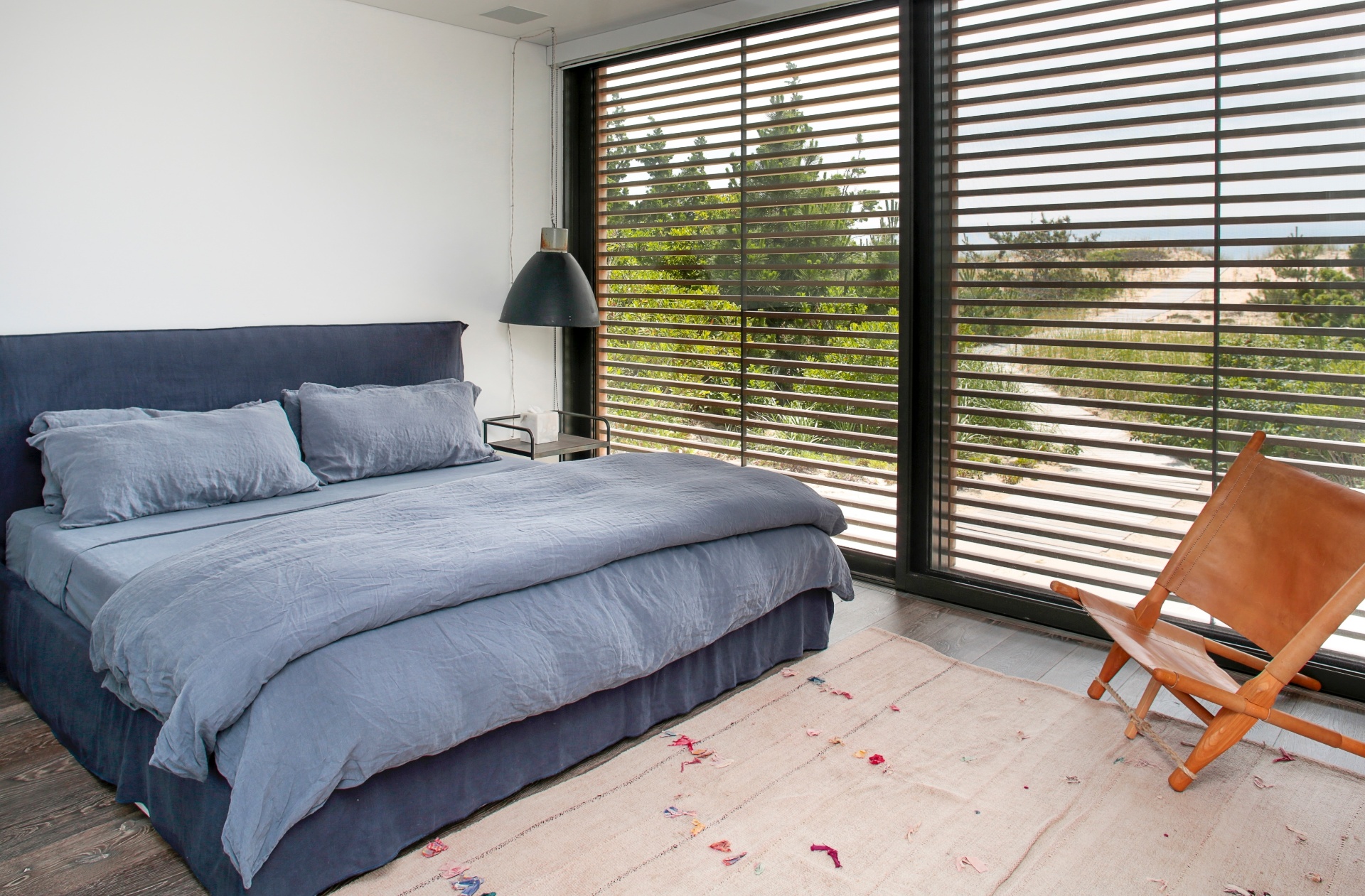 (Imagem do NYT, usar apenas no respectivo material) Um dos quartos na ala de hóspedes está mobilado de forma simples, com uma cadeira de couro "vintage" Saw (à dir.), de autoria de Ole Gjerlov-Knudsen. As portas ripadas abrem completamente e dão acesso à praia - Eric Striffler/ The New York Times