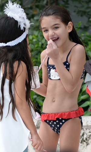 30.dez.2013 - Com um biquíni da Hello Kitty, Suri faz graça com um pirulito, ao passar a tarde em uma piscina em Miami com a mãe e uma amiguinha