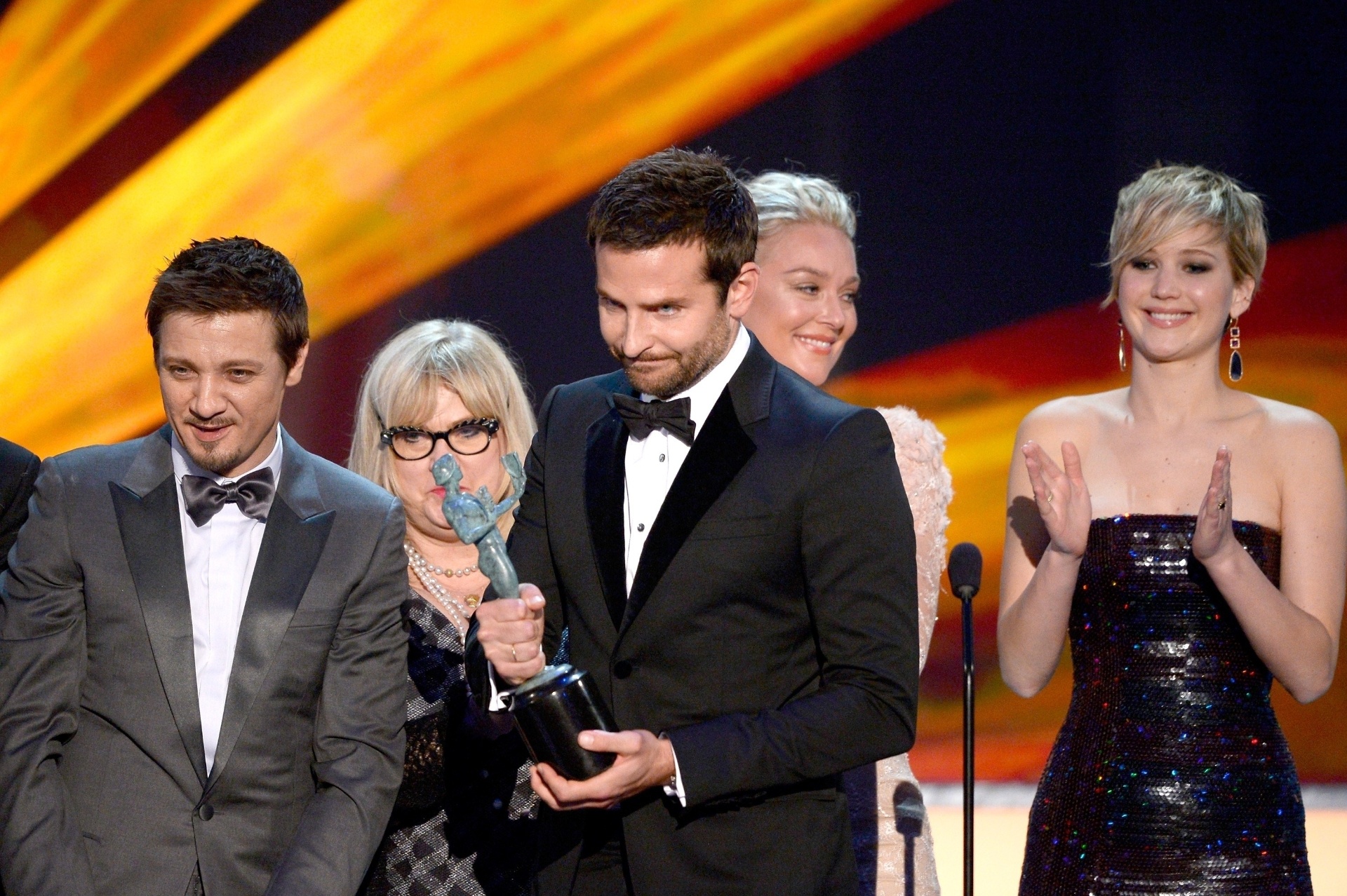 18.jan.2014 - Bradley Cooper segura o prêmio cercado dos atores Jeremy Renner e Jennifer Lawrence, e da equipe de "Trapaça". O filme de David O. Russell venceu o prêmio de melhor elenco, batendo "12 Anos de Escravidão" - KEVORK DJANSEZIAN/AFP