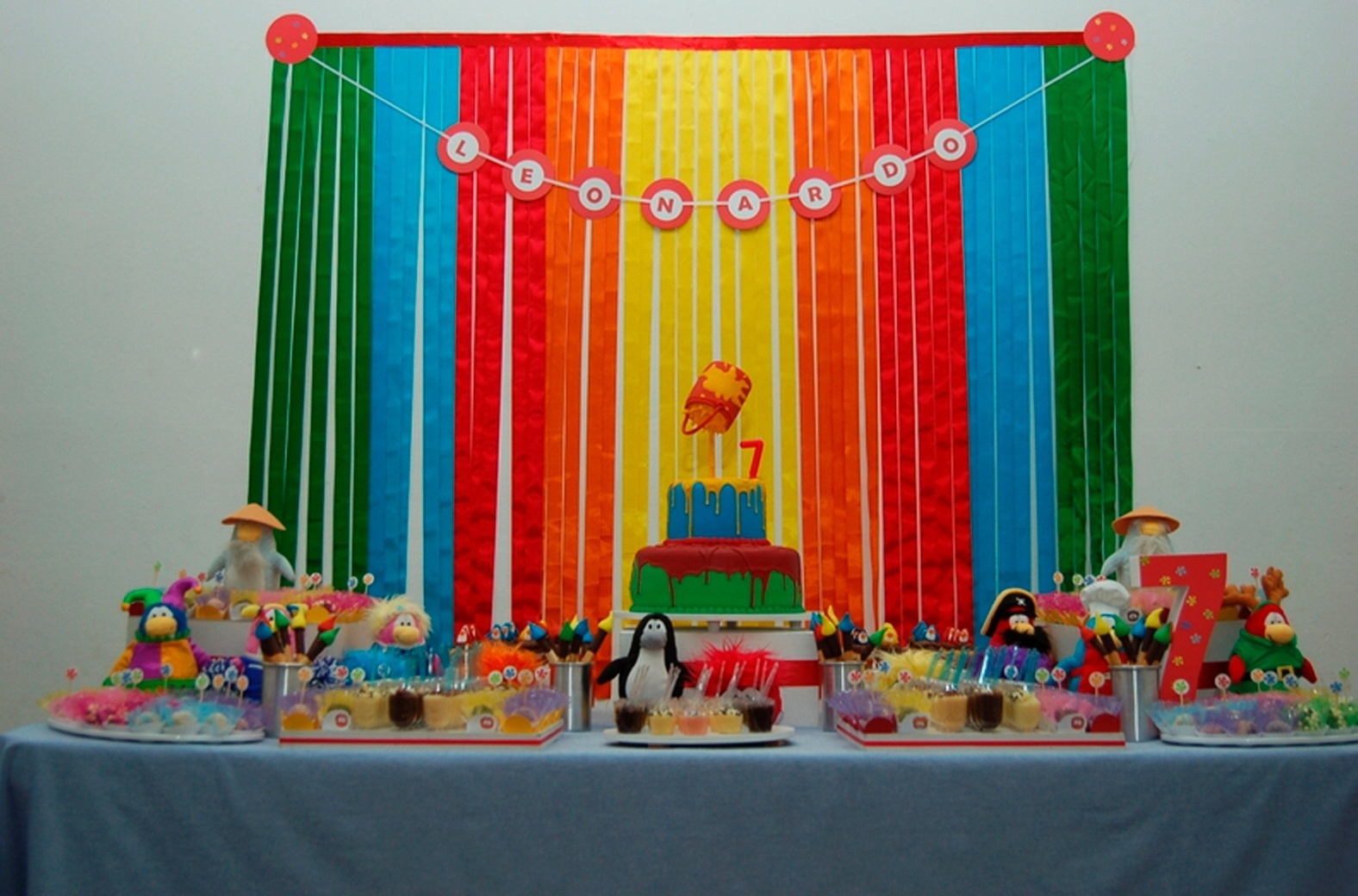 No aniversário com o tema do jogo "Club Penguin", a empresa Arquitetas da Festa (www.arquitetasdafesta.com.br) montou um painel com fitas de cetim coloridas. O nome do aniversariante foi confeccionado em papel colorset e sulfite. Para decorar a mesa, a empresa usou personagens de pelúcia - Divulgação