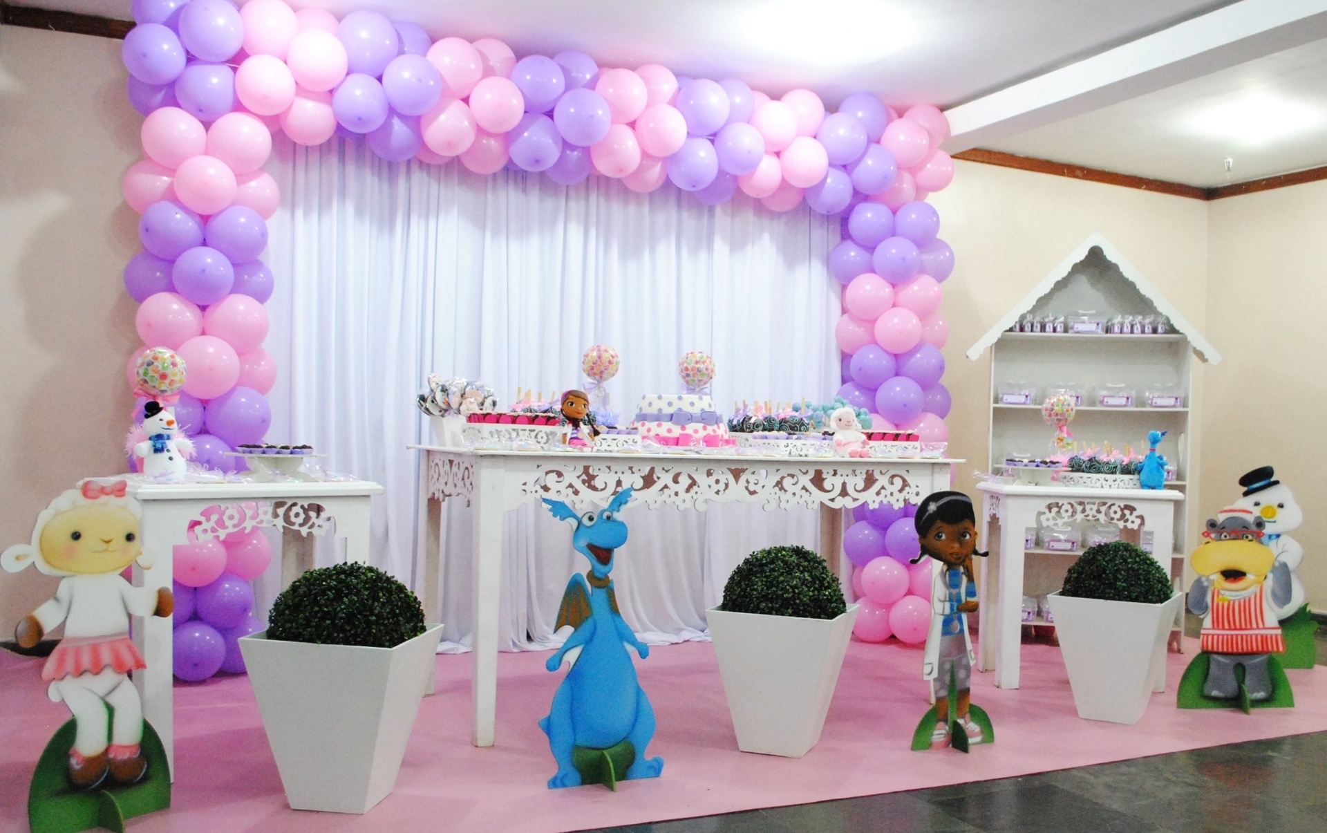 Para compor a decoração de aniversário com o tema Doutora Brinquedos, a equipe da Sky Festas(www.facebook.com/sky.festas) usou cortina branca, tapete rosa e móveis em estilo provençal. Os personagens do desenho, confeccionados em MDF, ficaram logo à frente, para recepcionar os convidados, ao lado dos vasos com buchinhos. Na mesa, um bolo de pasta americana e árvores de jujuba se misturavam às maçãs do amor decoradas, aos brigadeiros e aos biscoitos - Divulgação