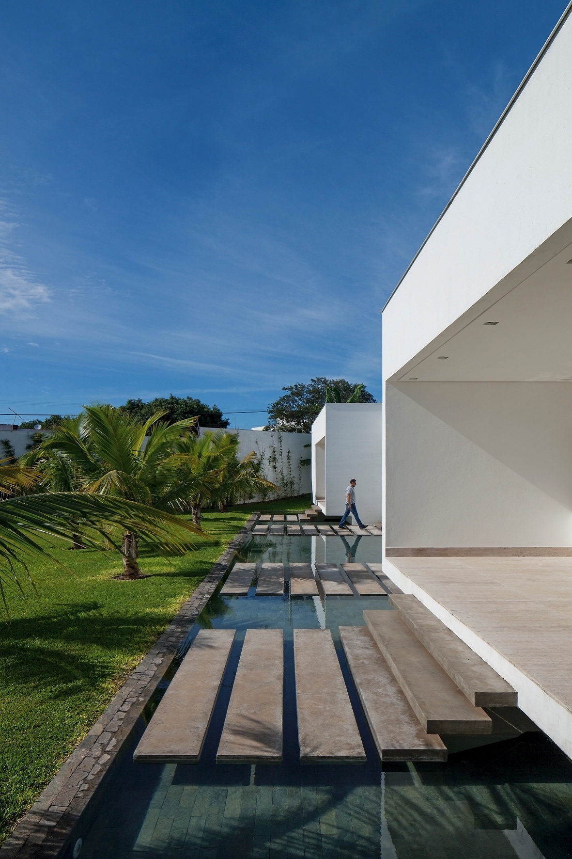 Aproveitando o suave desnível do terreno, criou-se um jardim e um espelho d?água que reflete o volume dos dormitórios, este elevado a 80 cm. O acesso aos quartos se dá por degraus apoiados em pilares centrais que dão a sensação visual de estarem flutuando - Leonardo Finotti/UOL