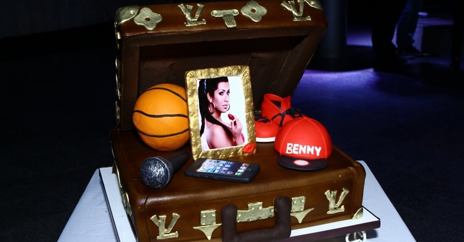 Detalhe para o bolo de aniversário de Naldo Benny em formato de maleta decorado com bola de basquete, par de tênis vermelho, um boné, um microfone e um porta retrato com a foto de sua mulher, Ellen Cardoso