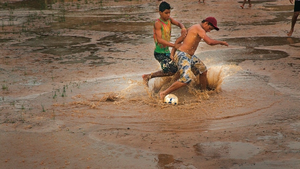 "O futebol de rua é como um ritual no Brasil ou uma religião. Faz parte da nossa vida", diz Vilela à BBC Brasil. Acima, dois jovens jogam em campo cheio de lama - Caio Vilela/Divulgação BBC