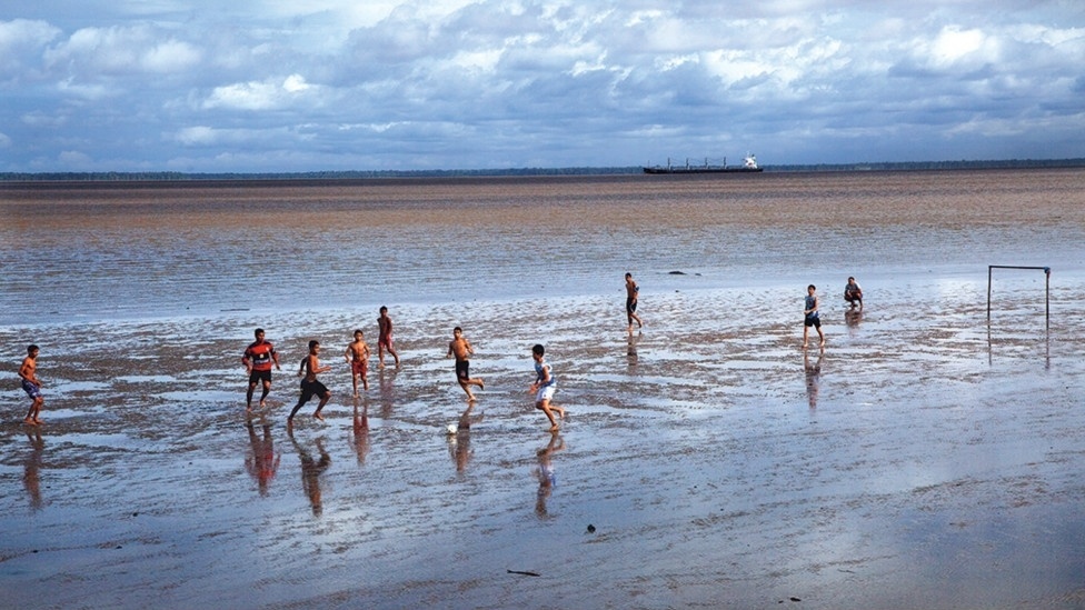 O livro é fruto de um projeto maior chamado "Futebol sem Fronteiras", idealizado por Vilela em 2004 e que conta com um acervo de imagens produzidas em 53 países. Acima, o famoso "futilama", jogado todo fim de tarde com traves móveis e sem chuteiras durante a maré baixa do rio Amazonas, em Macapá, no Amapá - Caio Vilela/Divulgação BBC