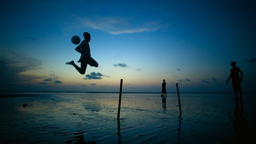 Uma paixão que começou no início da década de 1880, antes do fim da escravidão, quando padres jesuítas e vicentinos trouxeram as primeiras bolas de capotão da Europa. Acima, um homem faz malabarismos com a bola no pôr do sol de Jericoacoara, no Ceará. - Caio Vilela/Divulgação BBC