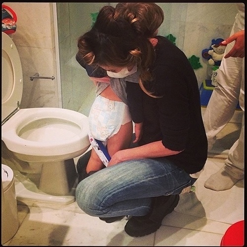 28.mai.2014 - De máscara, Luciana Gimenez leva o filho mais novo, Lorenzo, ao banheiro e troca a fralda dele