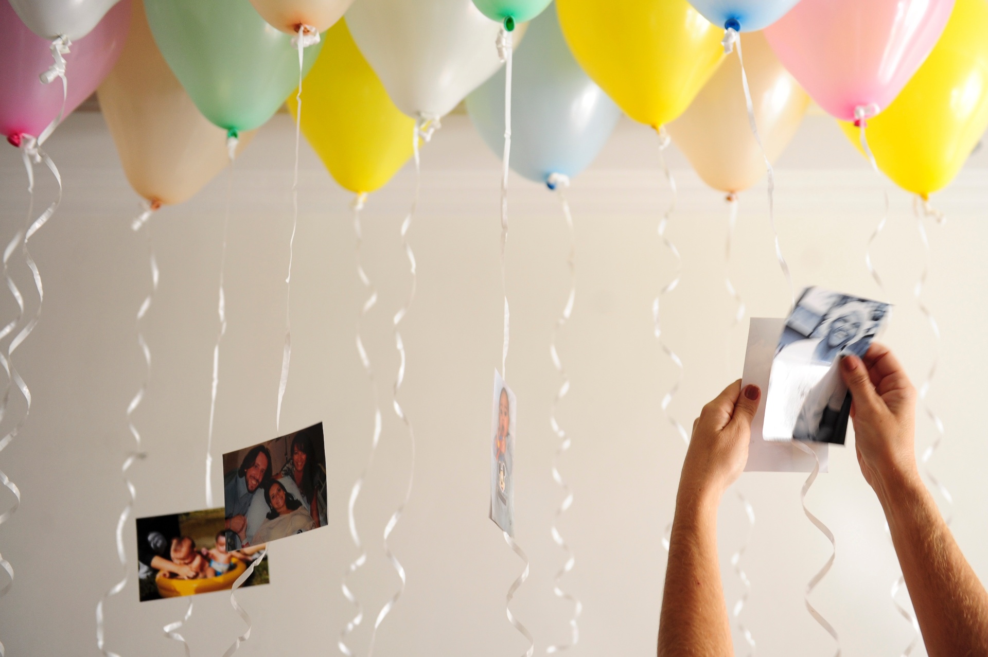 Faça um "sanduíche" com duas fotos de mesmo tamanho, com o fitilho no meio. Se não quiser gastar com gás hélio, você pode encher a bexiga normalmente e, no topo dela, colocar um pedaço de fita crepe para fixá-la no teto - Junior Lago/UOL