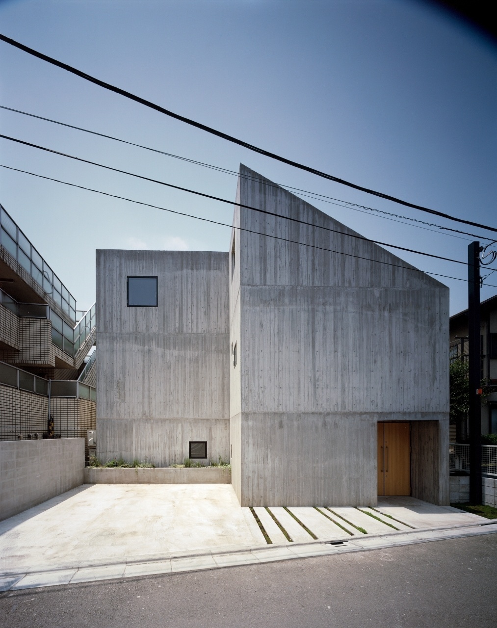 A fachada da Casa TN, do arquiteto japonês Tsuyoshi Ando, mantém uma linguagem sóbria, geométrica e que preza pela privacidade de seus moradores. A entrada de luz natural não se dá pelas janelas voltadas para a rua, mas por claraboias na cobertura e através de vãos envidraçados junto ao pátio interno (quintal). Da rua, o que se vê são paredes de concreto aparente e uma garagem para dois carros - Kai Nakamura/ Divulgação