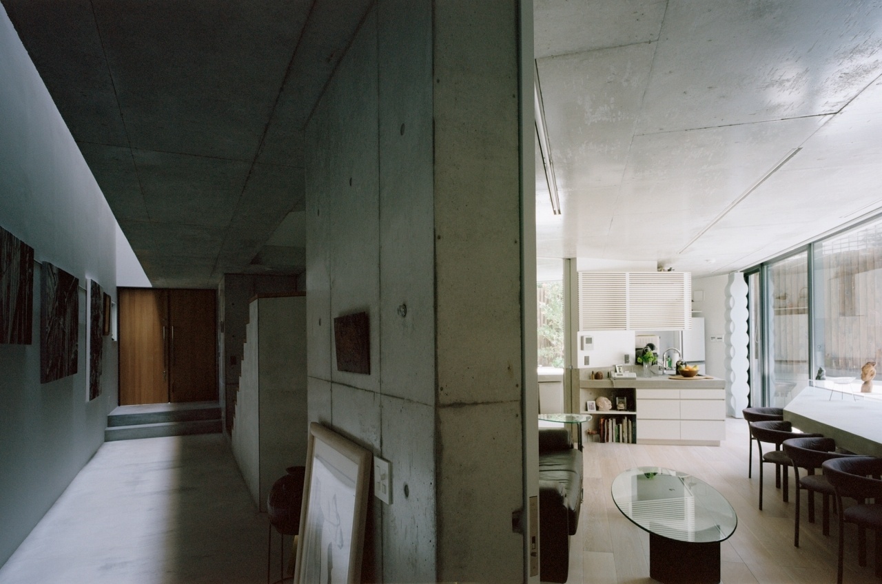 No andar térreo, de um lado, estão expostas as gravuras da matrona residente na Casa TN, do outro, separada por espessa parede estrutural de concreto armado modulado em fôrmas, fica a área social da morada desta senhora com cozinha integrada às salas de jantar e estar. Dos dois lados, o forro expõe irregularidades e a textura do concreto lixado e resinado. Arquitetura é de Tsuyoshi Ando - Kai Nakamura/ Divulgação