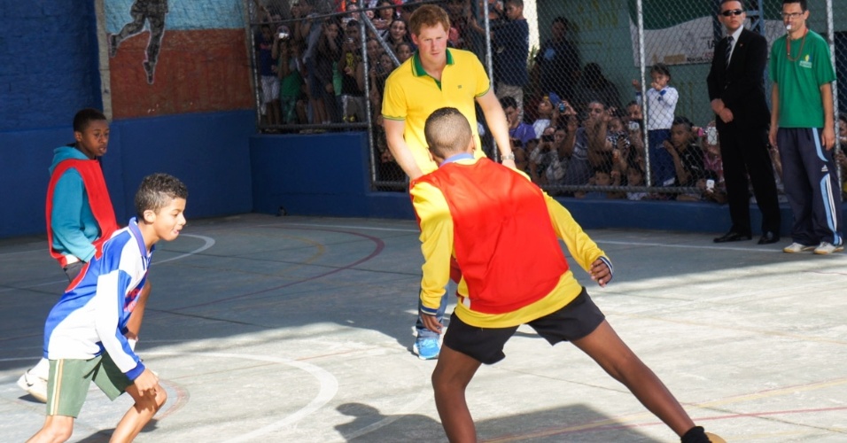 25.jun.2014 - Com a camisa do Brasil, Príncipe Harry joga futebol com crianças de projeto social em Diadema. Usando calça jeans e tênis, ele arriscou uns dribles em quadra na cidade paulista
