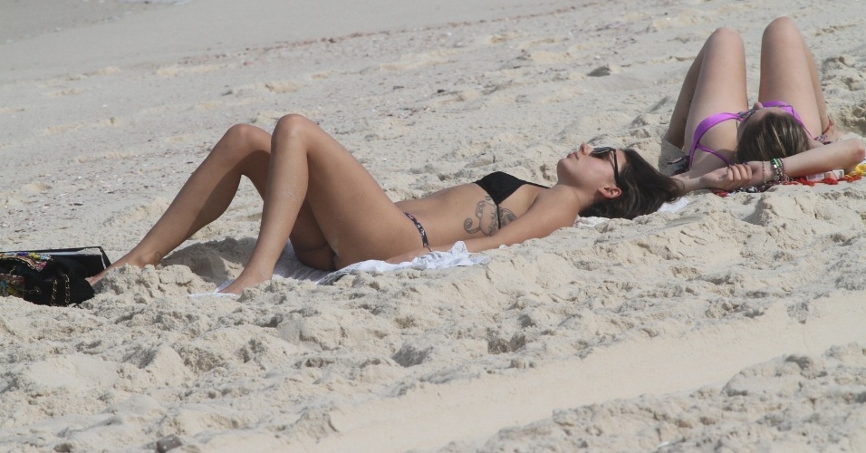 26.jun.2014 - De biquíni preto, Isis Valverde toma sol com amiga na praia da Reserva, no Rio de Janeiro