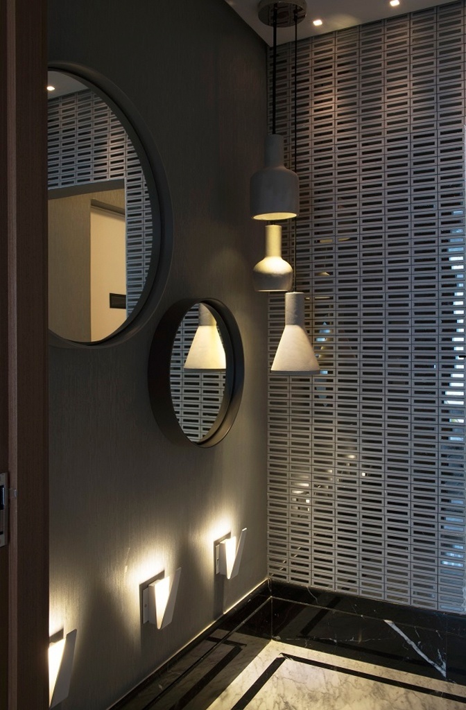 O hall social do apartamento decorado pela dupla Fernanda e Mariana Mattos recebeu tons escuros tanto no papel de parede, quanto na moldura do piso em pedra. Como o ambiente não é banhado pela luz natural, de acordo com as arquitetas, a iluminação correta foi importante para o não achatamento do espaço - Marcelo Magnani/ Divulgação