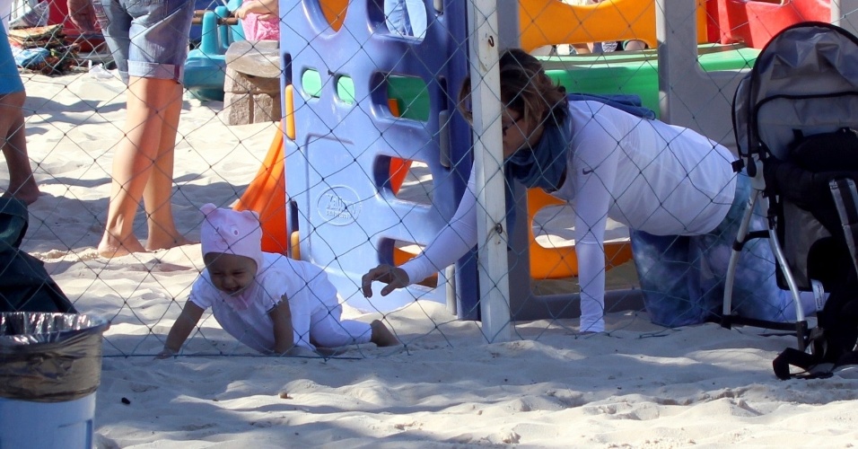 23.jul.2014 - Guilhermina Guinle brinca de pegar a filha Minna, que usa um gorro de bichinho, no parquinho infantil da praia de Ipanema, na zona sul do Rio