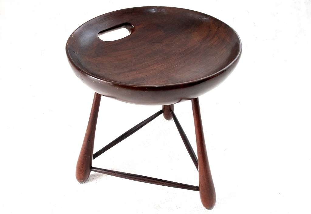 Banco Mocho. A peça de 1954 tem estrutura de madeira de lei maciça, três pés e assento esculpido em uma peça única. Existem versões em outros tons, como preto e verniz mais claro, e com estofado. O Mocho é a primeira peça industrializada e vendida na Oca, empresa criada pelo designer que produzia e comercializava suas criações - Aline Arruda/ UOL