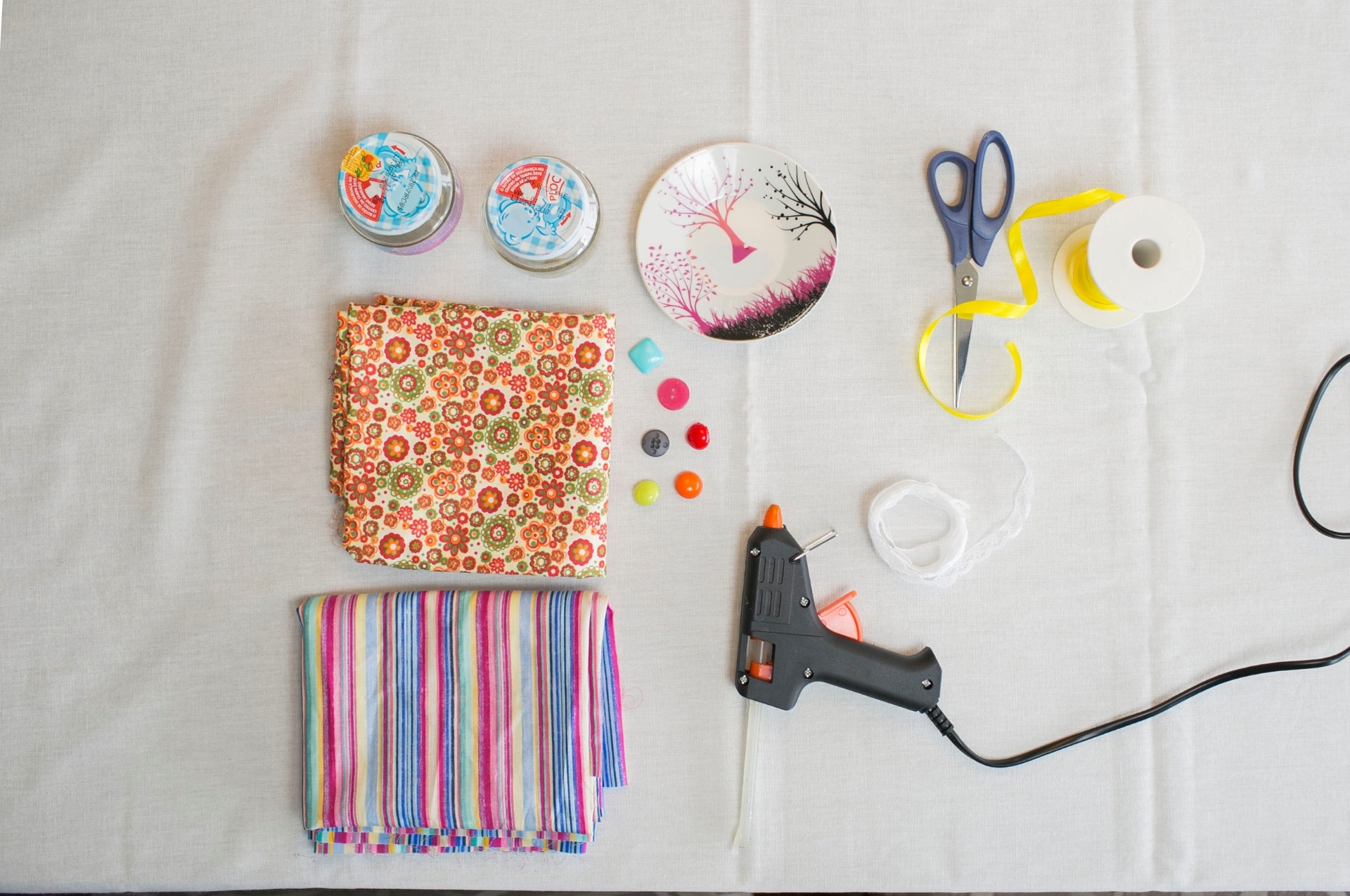 passo a passo de lembrancinha de aniversário com pote de papinha | Confira a seguir os materiais necessários para fazer a lembrancinha de aniversário: potinhos de papinha; pires pequeno; tesoura; fitas; tecidos; botões; renda; pistola de cola quente e lápis preto - Leonardo Soares/UOL