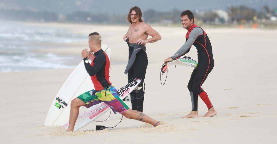 23.out.2014 - Na praia da Reserva, Paulinho Vilhena se alonga ao lado de Rômulo Neto e amigo na areia, antes de surfar