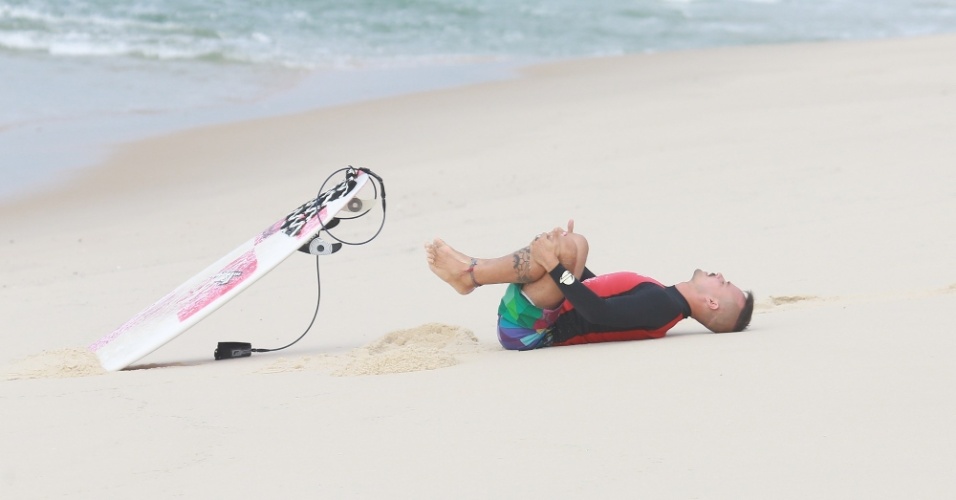 23.out.2014 - Paulinho Vilhena se alonga na areia antes de surfar na praia da Reserva, no Rio.