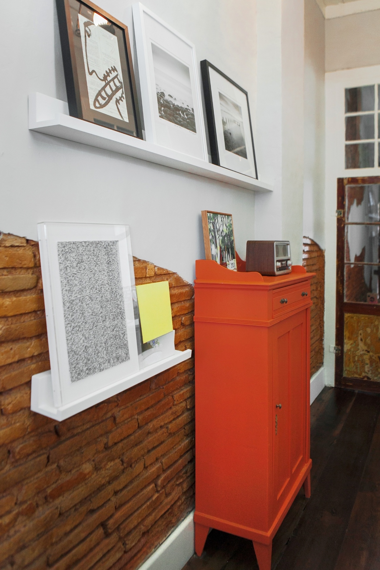 No corredor, sobre as prateleiras, estão apoiados quadros com fotos e ilustrações de artistas catarinenses - as obras são fornecidas pela galeria Helena Fretta. A cômoda de antiquário, também reformada e laqueada na cor laranja, entra em sintonia com o tom avermelhado dos tijolos a vista. A construção remonta ao período colonial, quando houve forte influência açoriana na arquitetura de Florianópolis (SC). O projeto de interiores para o Sobrado 505 é do Studio UM - Mauri Cherobin/ Divulgação