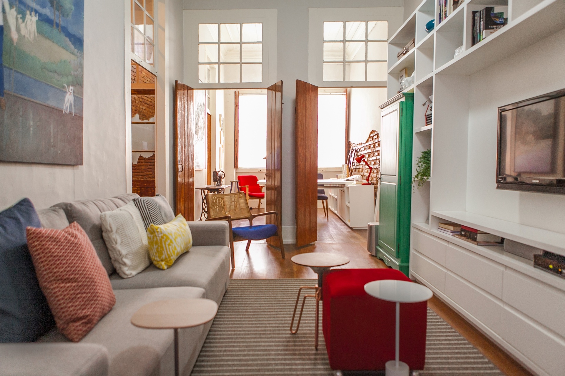 Pisos, portas e janelas foram recuperados no Sobrado 505, com reforma assinada pelo Studio UM. Já o reboco velho das paredes, onde estava intacto e sem umidades, foi mantido e apenas pintado com tinta acrílica comum. A área social é integrada por dois vãos de antigas portas, que permitem a passagem completa da luz natural desde a janela frontal da casa (fundo do escritório) até os fundos da sala de TV (em primeiro plano). A residência fica em Florianópolis (SC) - Mauri Cherobin/ Divulgação