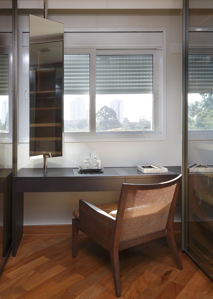 A arquiteta Viviane Cristina criou o closet com uma bancada posicionada logo abaixo da janela, entre os armários planejados da Florense. A mesa funciona como penteadeira e é complementada pelo espelho articulado (à esq.) posicionado de forma a não atrapalhar a abertura da janela e fornecer qualidade de imagem ao ser utilizado. O tampo do móvel é transparente, para facilitar a busca por maquiagens e bijuterias - Evelyn Müller/ Divulgação