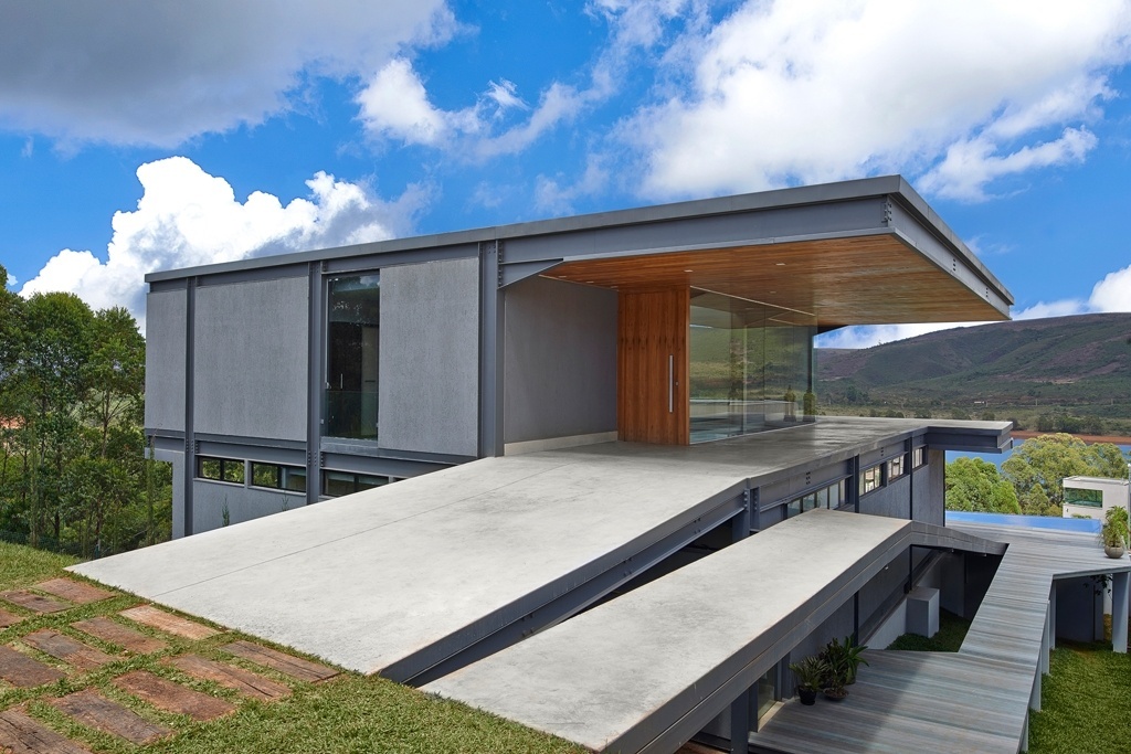 A circulação principal da Casa Península dos Pássaros, projetada pelos arquitetos Eduardo França e Letícia de Azevedo, em Nova Lima (MG), se dá por rampas. No mesmo nível da rua (mais alto), o acesso em concreto polido nível zero (muito liso, com aspecto de cimento queimado) cria um corredor lateral, que serve de garagem. A porta de entrada, de madeira ipê (a mesma dos forros), se abre para uma caixa de vidro que é o hall de distribuição para os cinco dormitórios - Jomar Bragança/ Divulgação