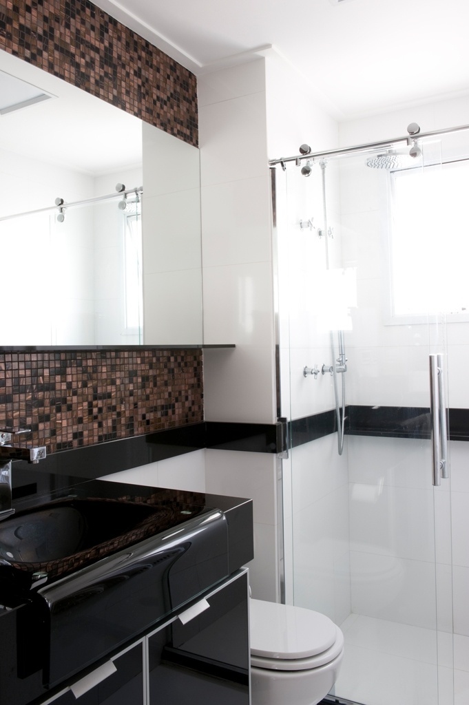 Para ganhar área e criar um ar sofisticado no banheiro com apenas três metros quadrados, o escritório Mattos Arquitetura recorreu a cubas ousadas, frontão percorrendo a parede e espelho na horizontal. O boxe com porta de correr também economiza espaço - Marcelo Magnani/ Divulgação