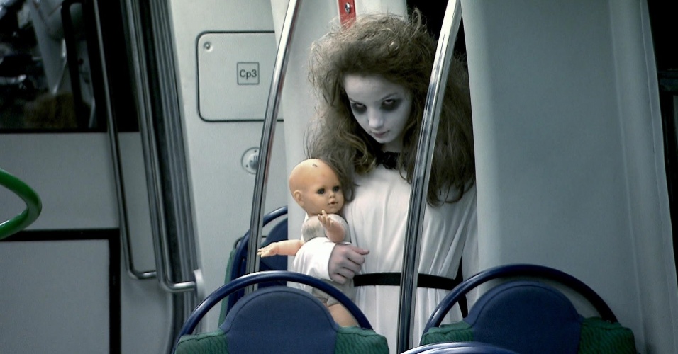 Após aterrorizar as pessoas no elevador, Menina Fantasma aparece no metrô, vestida de branco, com megahair no cabelo, maquiagem branca e uma boneca nas mãos assustando as vítimas em um vagão