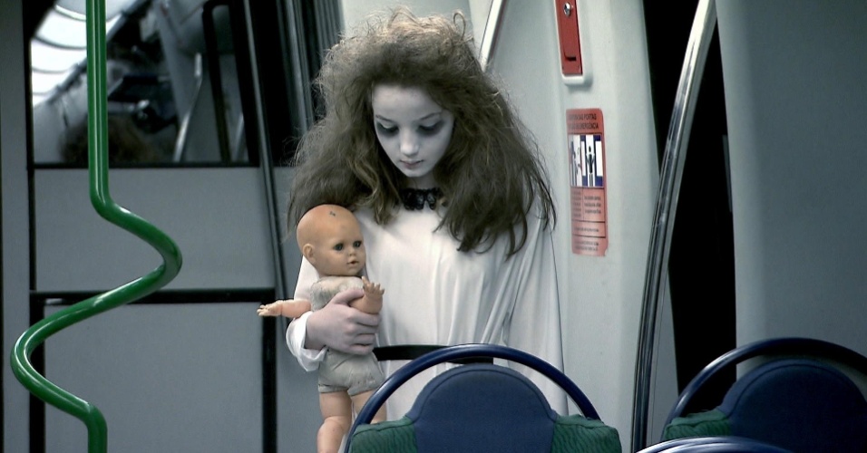 Meina Fantasma aparece no metrô, vestida de branco, com megahair no cabelo, maquiagem branca e uma boneca nas mãos