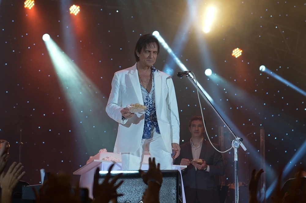 18.abr.2015 - Depois de ouvir a plateia cantando animadamente o "Parabéns a Você", puxado por sua própria banda, Roberto Carlos cortou vários pedaços de bolo no palco e levou um dos pratinhos para um felizardo na plateia - Francisco Cepeda/AgNews