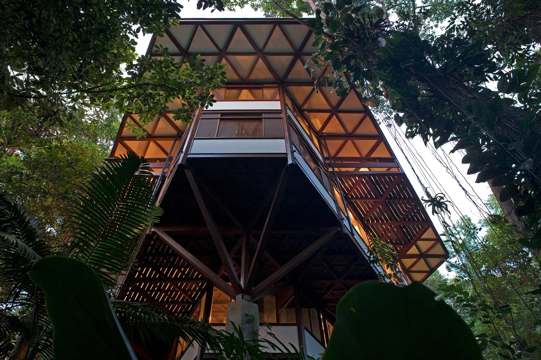 Esse ângulo favorece a observação do sistema de transição da estrutura de madeira para o pilar de concreto. No pavimento superior destaca-se o formato "bay-window" (espécie de janela saliente que sobressai na fachada) dos dormitórios e, acima, do estar. Coroando a edificação está o piso em balanço da cobertura. A casa Tijucopava foi projetada pelo arquiteto Marcos Acayaba - Leonardo Finotti/ UOL