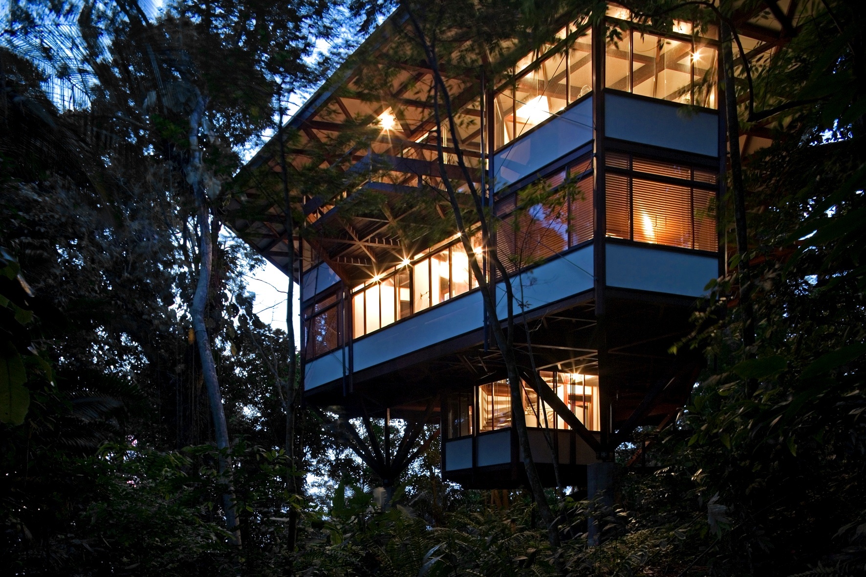 Ao cair da tarde, a silhueta da casa Tijucopava, projetada pelo arquiteto Marcos Acayaba, tem seus contornos emoldurados pela densa vegetação local. Destaques para o balanço da cobertura e dos peitoris brancos em madeira compensada - Leonardo Finotti/ UOL