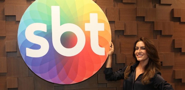 Ticiana Villas Boas posa ao lado do logo do SBT após assinar contrato com a emissora para apresentar um reality culinário