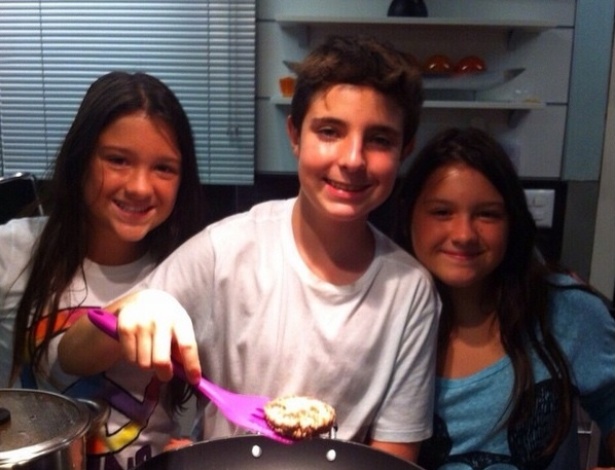 João Augusto, de 13 anos, prepara o jantar com as irmãs gêmeas na cozinha de sua casa