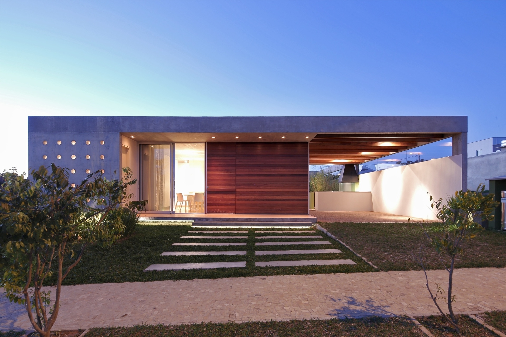 A fachada frontal da casa Madrid, projetada pela arquiteta Monica Drucker, exibe muitas aberturas. Como a residência ocupa toda a largura do terreno, as janelas laterais foram dispensadas e as aberturas se concentraram na frente e nos fundos. À esquerda, a parede perfurada leva luz à cozinha. Os orifícios foram moldados com tubos de PVC e receberam caixilharia pequena com aro de alumínio e vidro basculante. A obra fica em Marília, interior de São Paulo - Ruben Otero/ Divulgação