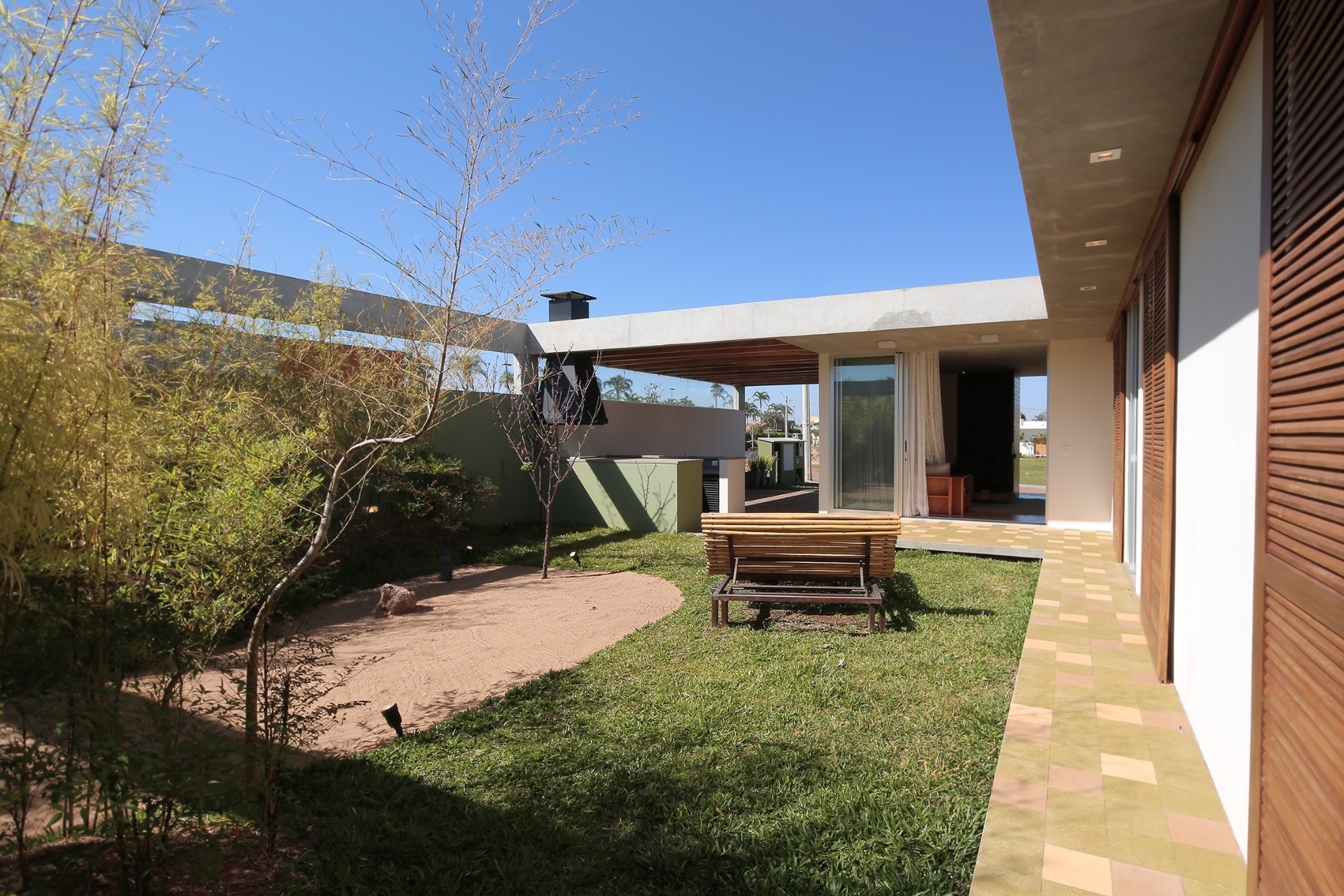 A casa Madrid conta com área verde abundante e todos os cômodos têm aberturas voltadas para ela. É "uma casa-pátio", como define a arquiteta Monica Drucker, que desenvolveu o conceito moderno, cuja base expressiva é o concreto aparente. Para  amenizar o calor intenso da região de Marília, interior de São Paulo, a implantação levou em conta estudos sobre a ventilação cruzada. Na área externa, ao redor do pátio, os piso são de ladrilho hidráulico foscos e naturais - Ruben Otero/ Divulgação