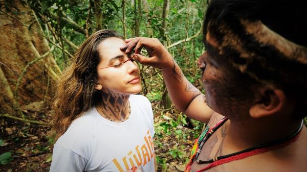 Liderança da aldeia Shanenawa, no Acre, pinta o rosto de uma turista durante ritual na floresta amazônica